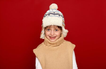 winter, child,  concept - happy girl in hat and sweater posing on red backgroundの写真素材