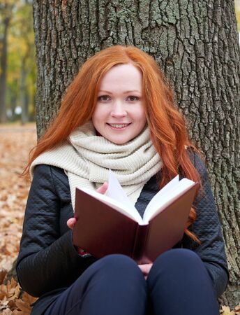 redhead girl read book in city park, fall seasonの写真素材
