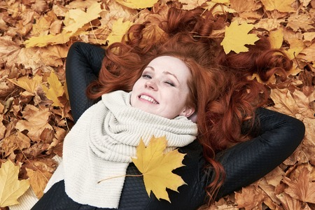 redhead girl lying on leaves in city park, fall seasonの写真素材