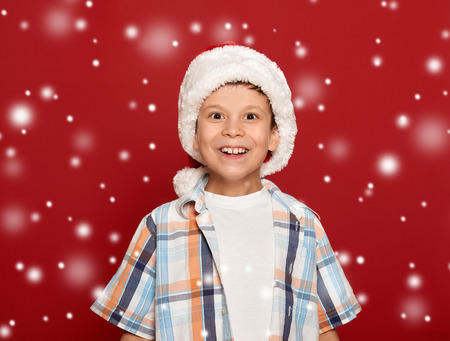 winter holiday christmas concept - boy in santa helper hat portrait on red backgroundの写真素材