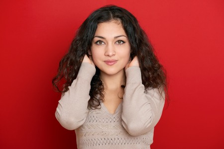 beautiful young woman portrait with black long curled hair on redの写真素材
