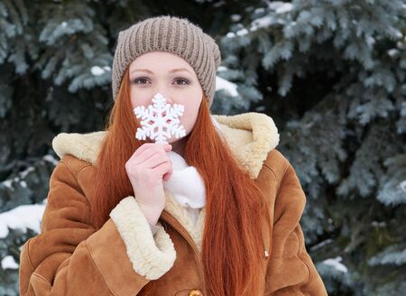 Girl portrait at winter forest, snowy weather, showing big snowflake toy.