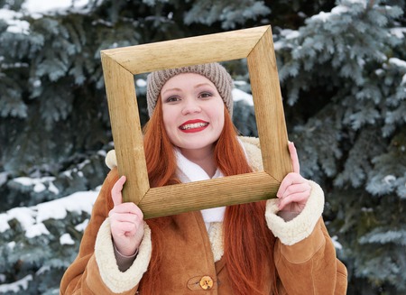 Woman outdoor portrait in wooden photo frame at winter . Snowy weather in fir tree forest.の写真素材