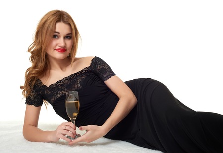 girl with glass of champagne lying on fur, wearing a black dress.の写真素材
