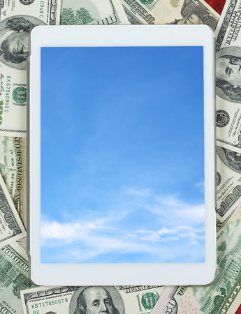 Tablet pc placed on center of money dollar and wood background, cloud sky on screen, business concept and information mockupの写真素材