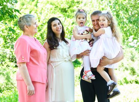 many generations family and pregnant woman in city park, summer season, green grass and trees
