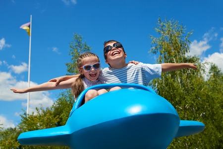 child girl and boy fly on blue plane attraction in city park, happy childhood, summer vacation conceptの写真素材