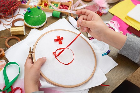 boy embroidered on the hoop, hand closeup and red ribbon on white textile, learns to sew, job...