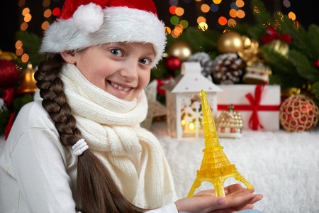 child girl portrait with eiffel tower and christmas decoration, dark background with lights, face expression and happy emotions, dressed in santa hat, winter holiday conceptの写真素材