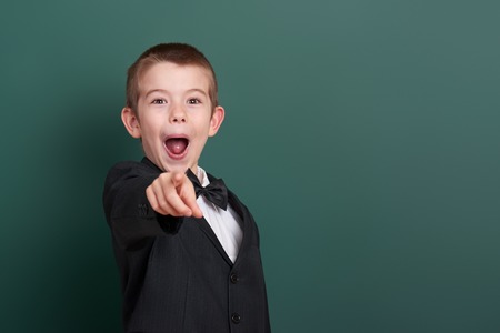 school boy point the finger near blank chalkboard background, dressed in classic black suit, group pupil, education conceptの写真素材
