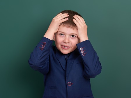 very emotional school boy portrait near green blank chalkboard background, dressed in classic black suit, one pupil, education conceptの写真素材