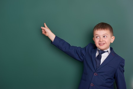 school boy point the finger near blank chalkboard background, dressed in classic black suit, group pupil, education conceptの写真素材