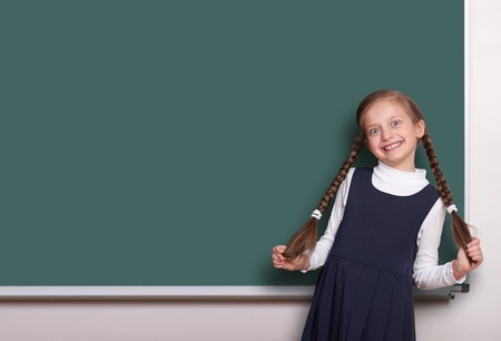 beautiful school girl with pigtail smiled near blank chalkboard background, dressed in classic black...