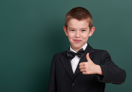 school boy show best gesture, portrait near green blank chalkboard background, dressed in classic black suit, one pupil, education conceptの写真素材