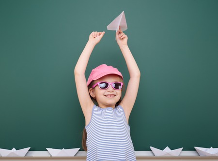 Schoolgirl with paper plane play near a blackboard, empty space, education conceptの写真素材