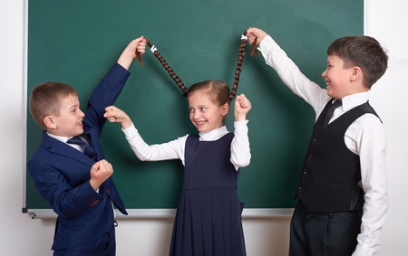 child play and having fun, boys pull the girl braids, near blank school chalkboard background, dressed in classic black suit, group pupil, education conceptの写真素材