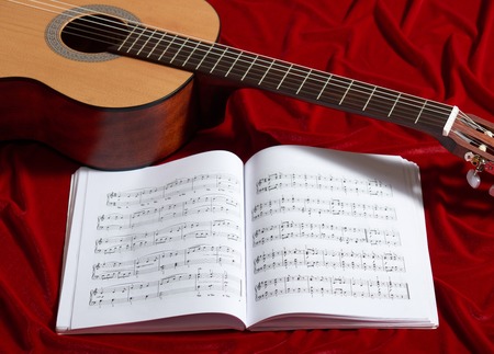 acoustic guitar and music notes on red velvet fabric, close view of objectsの写真素材