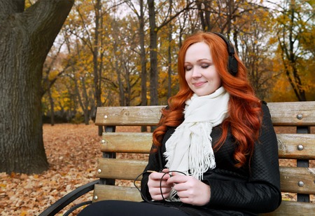young woman portrait in autumn park, listening to music on headphonesの写真素材