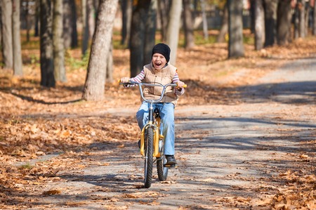 boy riding on Bicycle in autumn Park, bright sunny day, fallen leaves on backgroundの写真素材