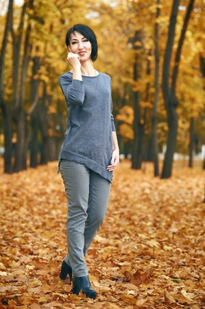 woman posing in autumn park with yellow trees, fall seasonの写真素材