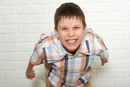portrait of a emotional boy standing near white brick wall, dressed in a plaid shirtの写真素材