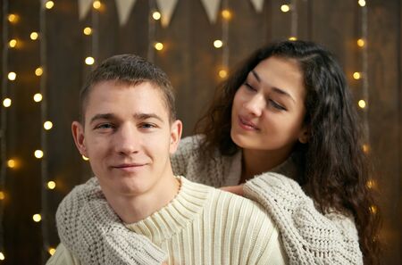 couple in christmas lights and decoration, dressed in white, young girl and man, fir tree on dark wooden background, winter holiday conceptの写真素材