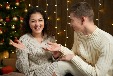 the man gives the girl an engagement ring, couple in christmas lights and decoration, dressed in white, fir tree on dark wooden background, winter holiday conceptの写真素材