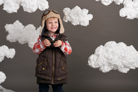 boy dressed as an airplane pilot stands between the clouds and looks through binocularsの写真素材