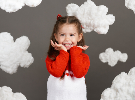 girl playing with clouds, dressed in red sweater, shot in the studio on a gray backgroundの写真素材