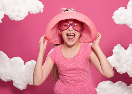 fashionable girl posing on a pink background with clouds, pink dress and hatの写真素材