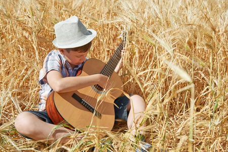 child with guitar is in the yellow wheat field, bright sun, summer landscapeの写真素材