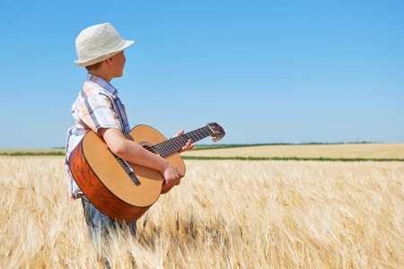 child boy with guitar is in the yellow wheat field, bright sun, summer landscapeの写真素材