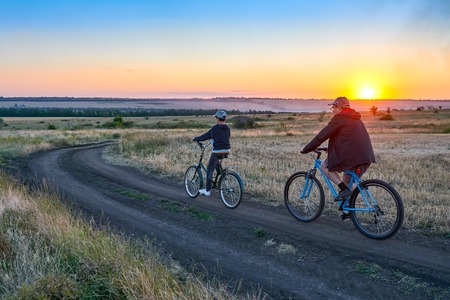 Father and son ride a bike in the country on the field in the evening
