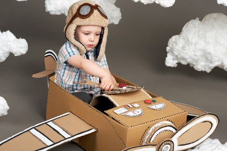 the boy plays in an airplane made of cardboard box and dreams of becoming a pilot, clouds from cotton wool on a gray background, retro styleの写真素材