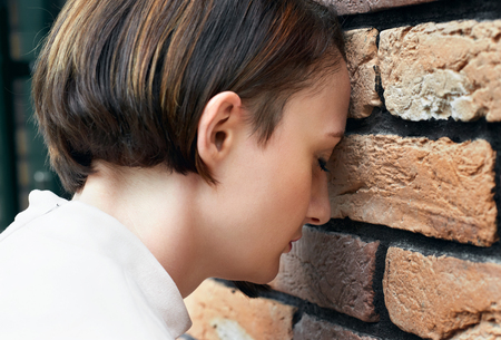 the young girl put her head to the brick wall, trouble conceptの写真素材