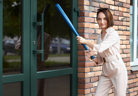 the girl stands at the closed door of the store and tries to break it with a baseball bat