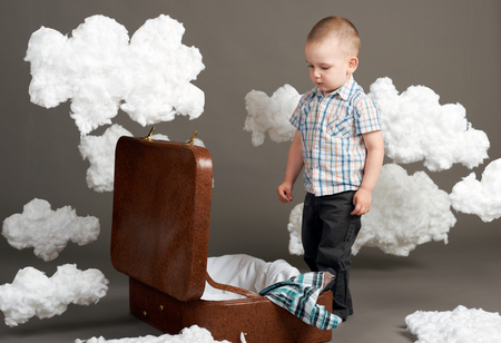 the boy is sitting in a suitcase and going on a journey, clouds of cotton wool as a decoration, gray backgroundの写真素材