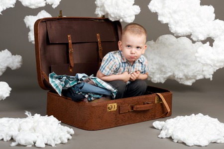 the boy is sitting in a suitcase and going on a journey, clouds of cotton wool as a decoration, gray backgroundの写真素材