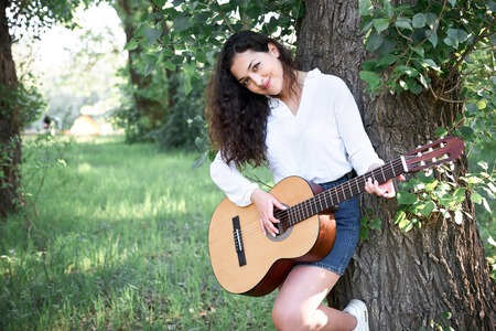young woman walking in the forest and playing guitar, summer nature, bright sunlight, shadows and...