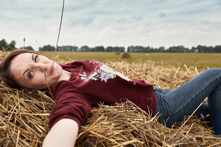 young girl having fun in the field, lying on a haystackの写真素材