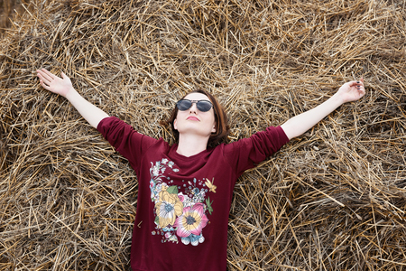 young girl having fun in the field, lying on a haystackの写真素材