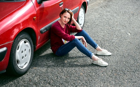 young girl sitting on the road by the red car