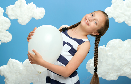 girl dressed in striped dress posing on a blue background with cotton clouds, white air balloon, the concept of summer and happinessの写真素材