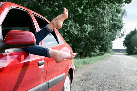 young woman driver resting in a red car, put her feet on the car window, happy travel conceptの写真素材
