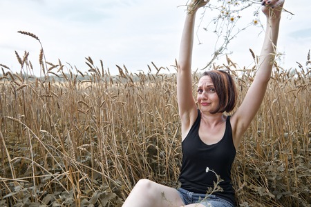 a young girl with a bouquet of flowers sitting near a wheat field. She picks off flower petals and wondering love or not love using old folk legends and traditions.の写真素材