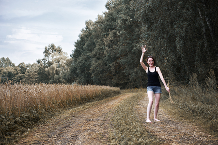 young girl throwing shoes, walking barefoot on dirt road through field and forest, summer and travel conceptの写真素材