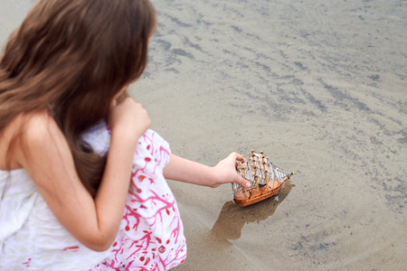 girl playing with a toy sailing ship by the riverの写真素材