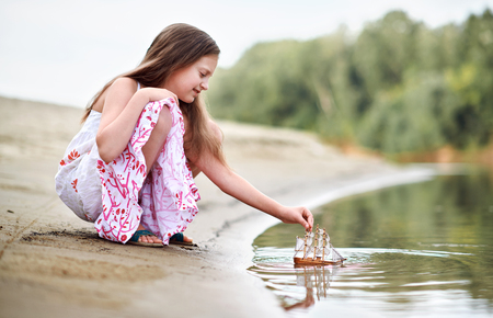 girl playing with a toy sailing ship by the riverの写真素材