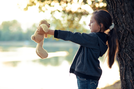 the girl child with toy bear is in the forest at sunset, beautiful river and landscapeの写真素材
