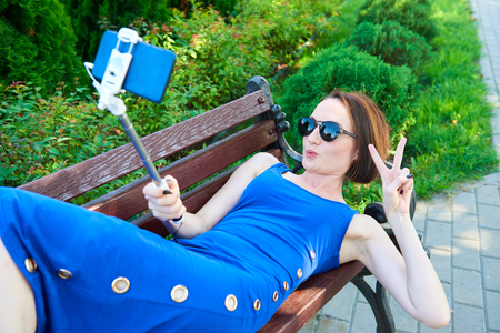 girl in a long blue dress lying on a bench in the city street, resting or taking a selfieの写真素材